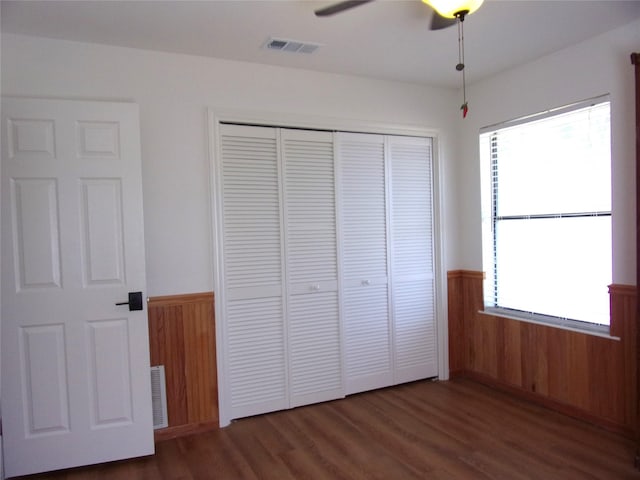 unfurnished bedroom with dark wood-type flooring, a closet, ceiling fan, and wood walls