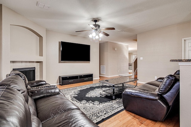 living area featuring a ceiling fan, wood finished floors, a fireplace, and visible vents