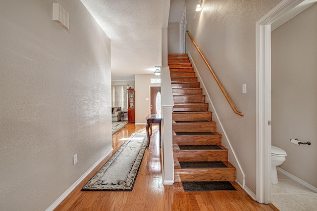 stairs with visible vents, wood finished floors, baseboards, and a textured ceiling