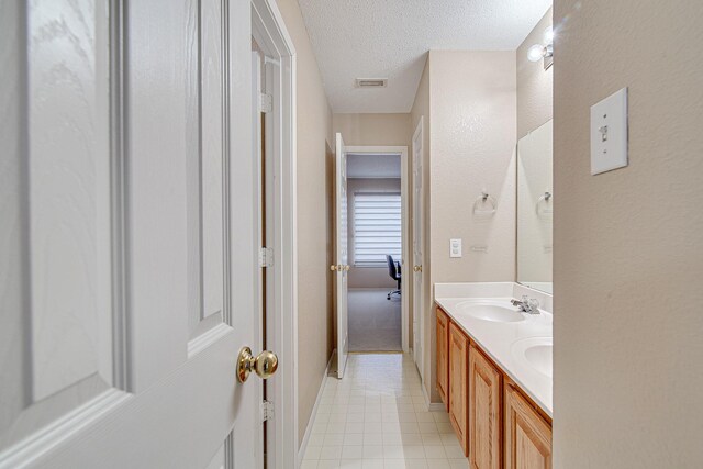 bathroom with double vanity, visible vents, a textured ceiling, and a sink