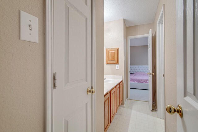 ensuite bathroom featuring vanity, ensuite bath, a textured wall, and a textured ceiling