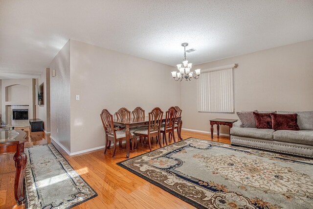 living area with light wood-type flooring, visible vents, an inviting chandelier, a fireplace, and baseboards