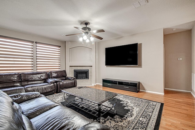 living area featuring visible vents, baseboards, a tiled fireplace, wood finished floors, and a textured ceiling