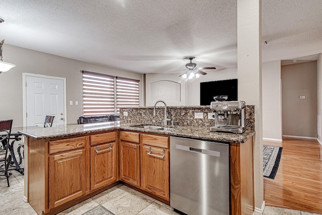 kitchen with brown cabinets, a ceiling fan, a sink, dark stone countertops, and dishwasher