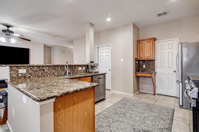 kitchen featuring backsplash, dark stone countertops, brown cabinets, appliances with stainless steel finishes, and a sink