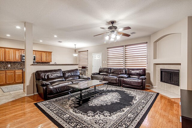 living room featuring a tiled fireplace, light wood-style flooring, visible vents, and a textured ceiling