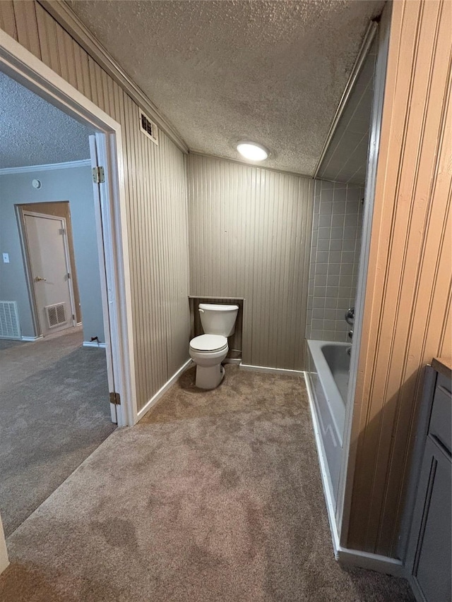 bathroom with toilet, crown molding, a textured ceiling, wooden walls, and a bathtub