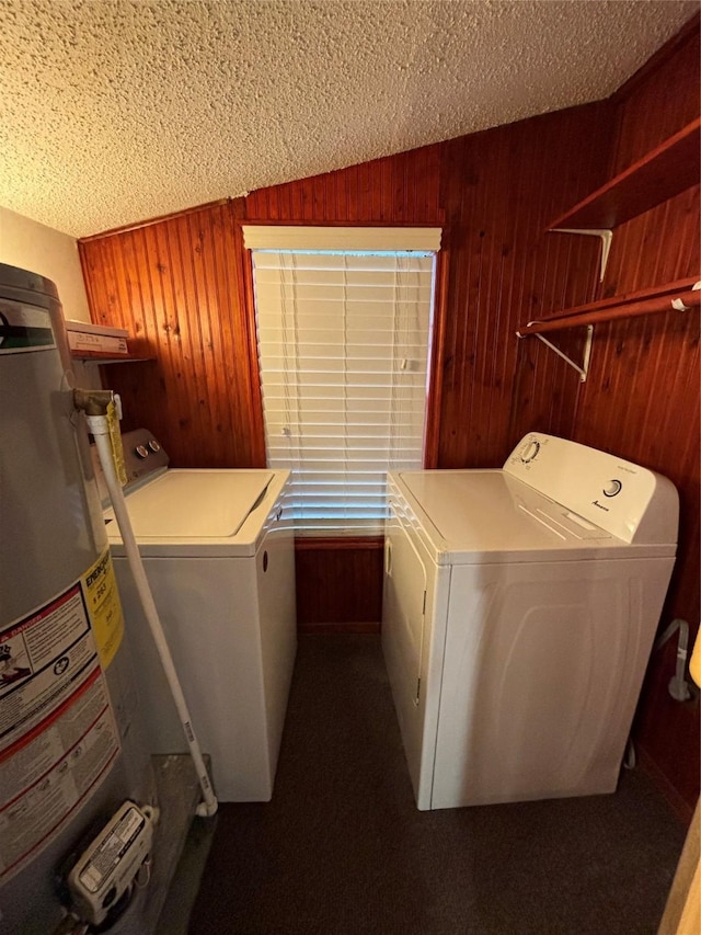 laundry area with gas water heater, washer and dryer, a textured ceiling, and wooden walls