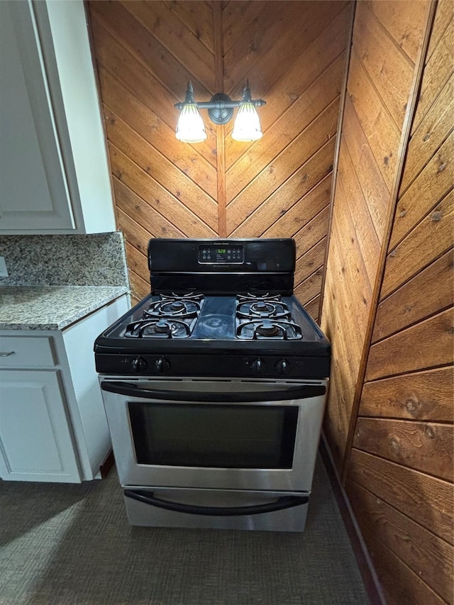 kitchen with white cabinetry, hanging light fixtures, light stone counters, gas range, and wood walls