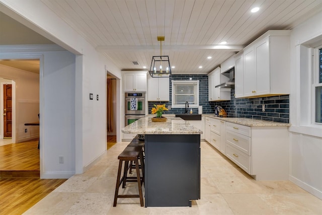 kitchen featuring hanging light fixtures, white cabinetry, a kitchen island, and wall chimney exhaust hood