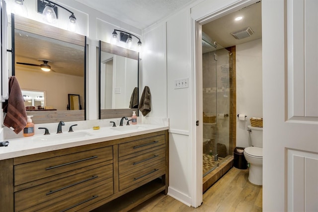 bathroom with toilet, a shower with shower door, vanity, ceiling fan, and hardwood / wood-style floors