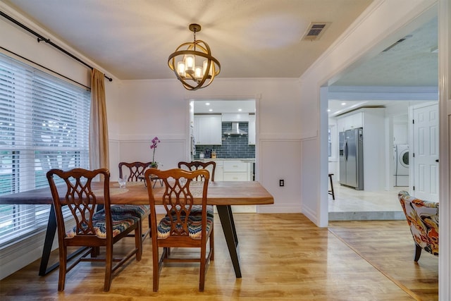 dining space featuring crown molding, washer / dryer, a chandelier, and light wood-type flooring