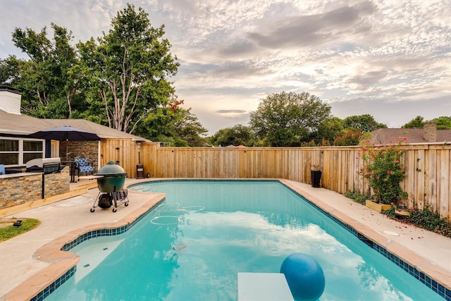 pool at dusk with a grill, a patio, and exterior kitchen