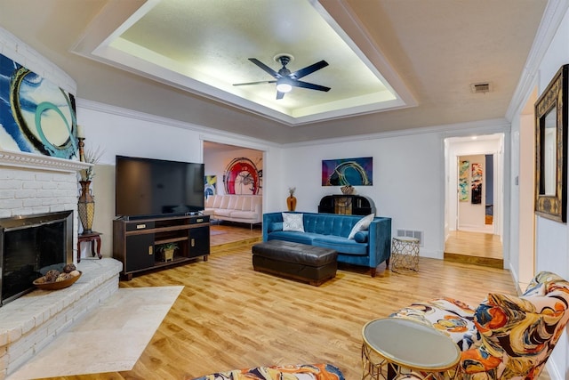 living room with a brick fireplace, a tray ceiling, and hardwood / wood-style flooring