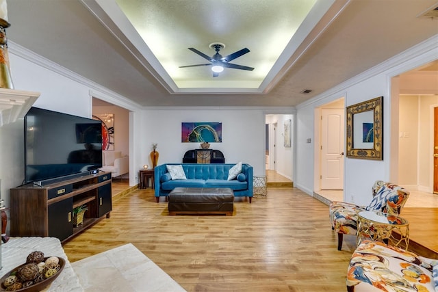 living room featuring ceiling fan, a tray ceiling, and light wood-type flooring