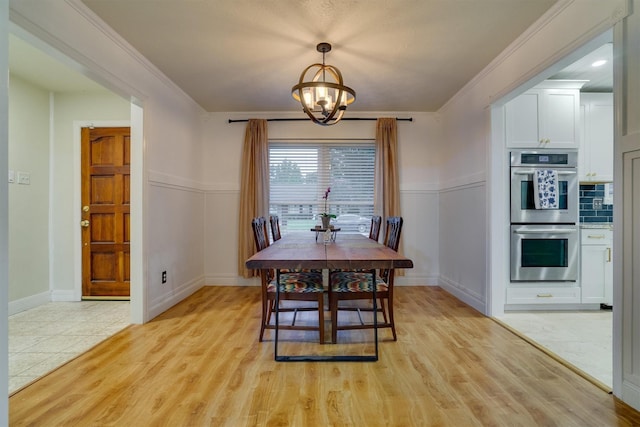 dining area with crown molding, an inviting chandelier, and light wood-type flooring