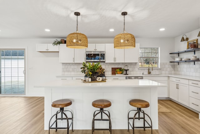 kitchen featuring sink, appliances with stainless steel finishes, white cabinetry, hanging light fixtures, and a kitchen bar