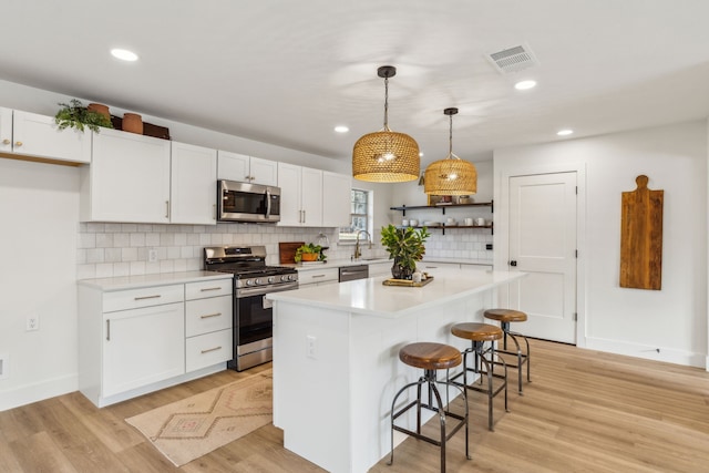 kitchen featuring a kitchen bar, white cabinetry, hanging light fixtures, appliances with stainless steel finishes, and a kitchen island