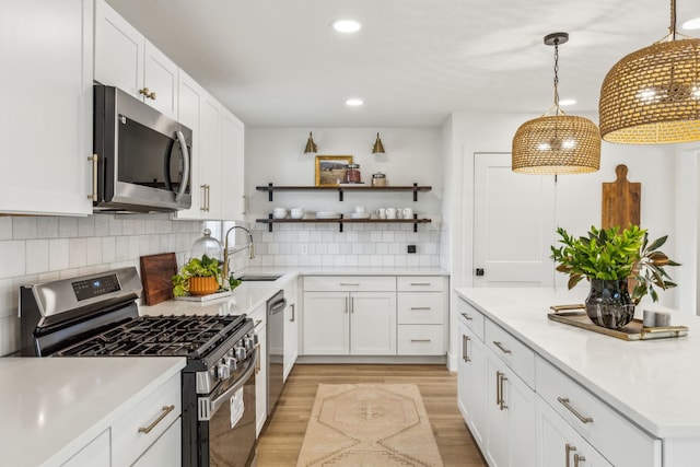 kitchen featuring sink, white cabinetry, hanging light fixtures, appliances with stainless steel finishes, and decorative backsplash