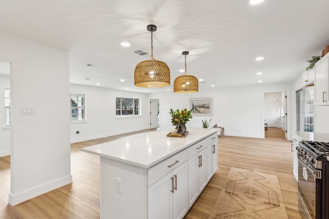 kitchen featuring pendant lighting, white cabinetry, a center island, stainless steel gas range oven, and light wood-type flooring