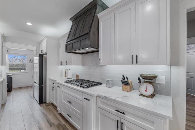 kitchen featuring white cabinetry, appliances with stainless steel finishes, light hardwood / wood-style floors, and premium range hood