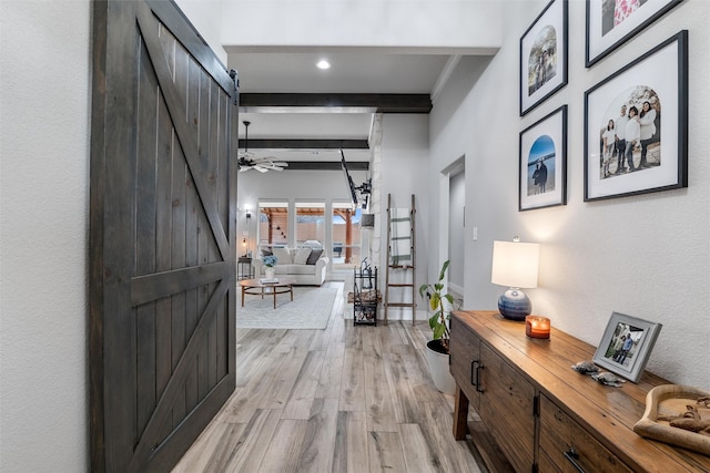 corridor featuring a barn door, beamed ceiling, and light wood-type flooring