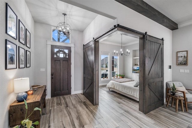 foyer featuring ornamental molding, a barn door, a notable chandelier, and light wood-type flooring