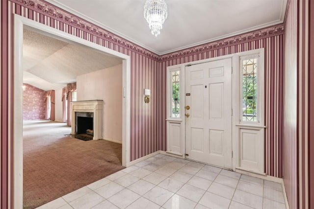 carpeted entryway with ornamental molding, a fireplace, vaulted ceiling, and a notable chandelier