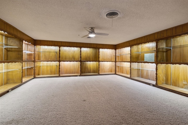 carpeted empty room with ceiling fan, wooden walls, and a textured ceiling