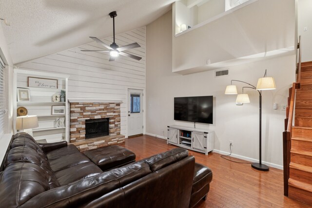 living room with a stone fireplace, a textured ceiling, wooden walls, ceiling fan, and hardwood / wood-style floors