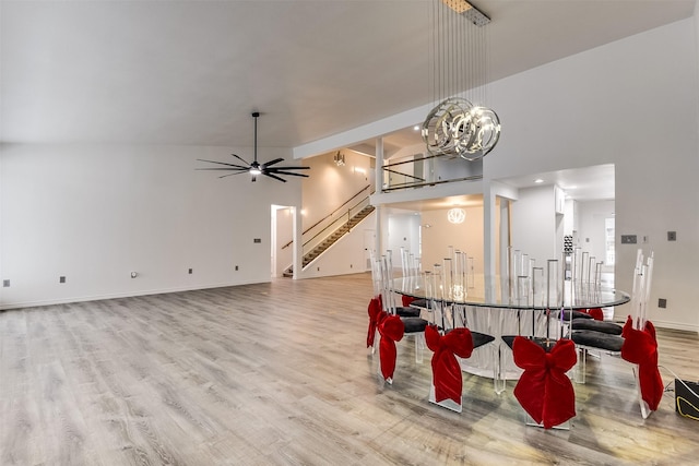 dining room with ceiling fan with notable chandelier, light hardwood / wood-style flooring, and a high ceiling