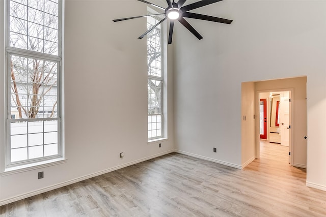 empty room with ceiling fan, light hardwood / wood-style floors, and a high ceiling