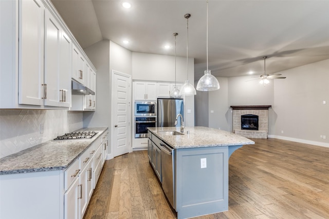 kitchen featuring an island with sink, white cabinets, hanging light fixtures, stainless steel appliances, and light stone countertops