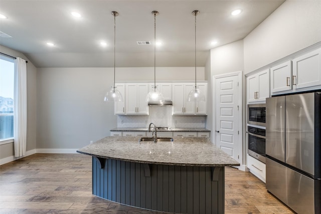 kitchen featuring sink, stainless steel appliances, an island with sink, white cabinets, and decorative light fixtures