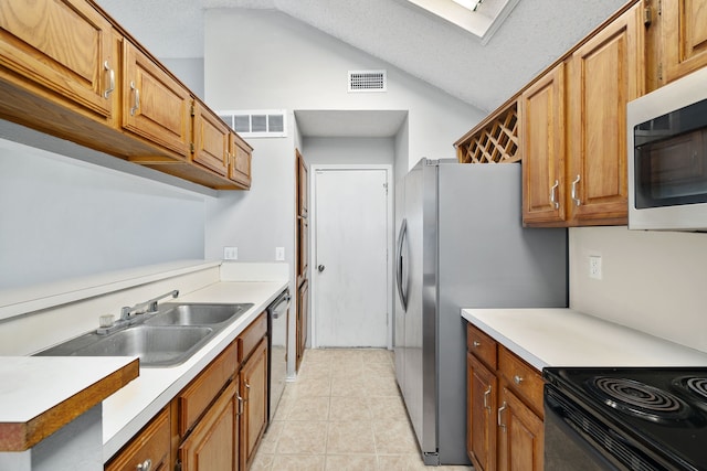 kitchen with lofted ceiling with skylight, appliances with stainless steel finishes, light tile patterned flooring, sink, and a textured ceiling