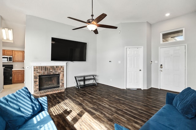 living room featuring a high ceiling, ceiling fan, a brick fireplace, and light wood-type flooring