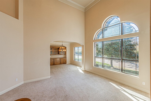 unfurnished living room with light colored carpet, ornamental molding, a high ceiling, and a notable chandelier