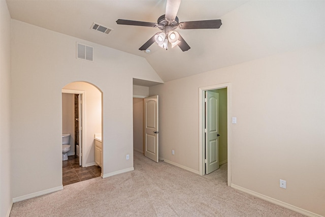 unfurnished bedroom with ensuite bath, vaulted ceiling, light colored carpet, and ceiling fan