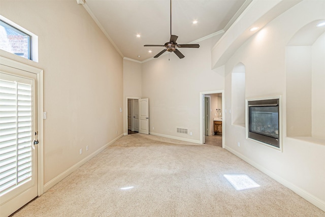 unfurnished living room with ceiling fan, ornamental molding, light carpet, and a high ceiling