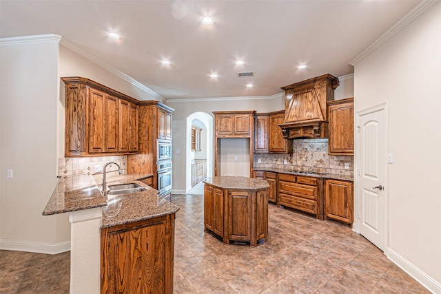 kitchen with sink, dark stone countertops, ornamental molding, appliances with stainless steel finishes, and a kitchen island