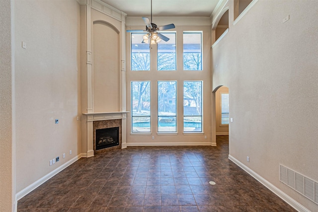 unfurnished living room with a fireplace, a towering ceiling, a wealth of natural light, and ceiling fan