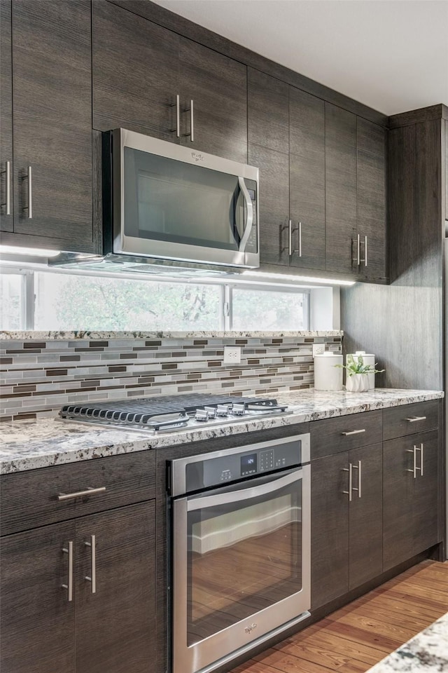 kitchen featuring light hardwood / wood-style flooring, appliances with stainless steel finishes, dark brown cabinets, tasteful backsplash, and light stone countertops