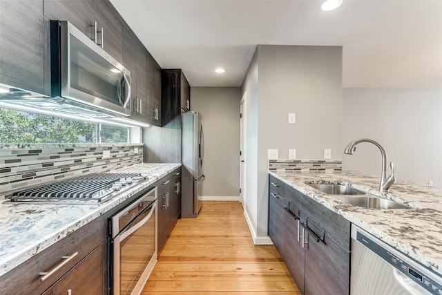 kitchen featuring sink, decorative backsplash, light stone counters, light hardwood / wood-style floors, and stainless steel appliances