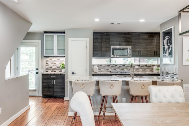 kitchen featuring sink, tasteful backsplash, light wood-type flooring, a kitchen breakfast bar, and a kitchen island with sink