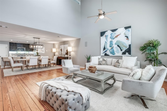 living room featuring hardwood / wood-style flooring, ceiling fan, and a towering ceiling