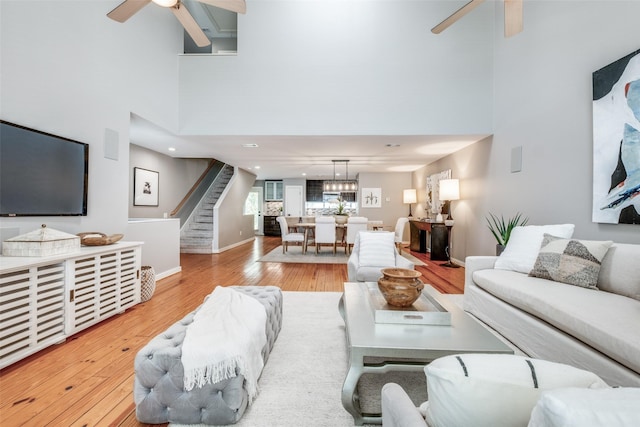 living room with ceiling fan, a towering ceiling, and light wood-type flooring