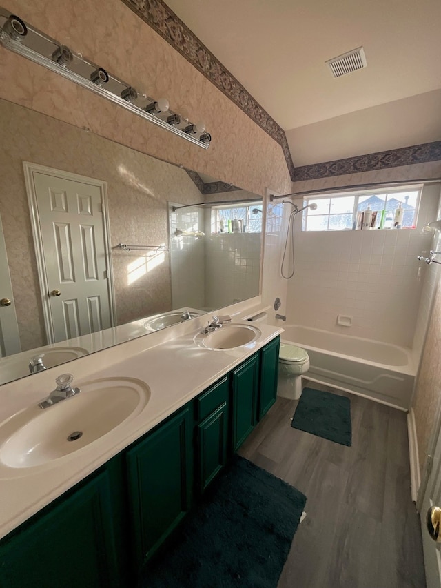 full bathroom with hardwood / wood-style floors, tiled shower / bath combo, vanity, vaulted ceiling, and toilet