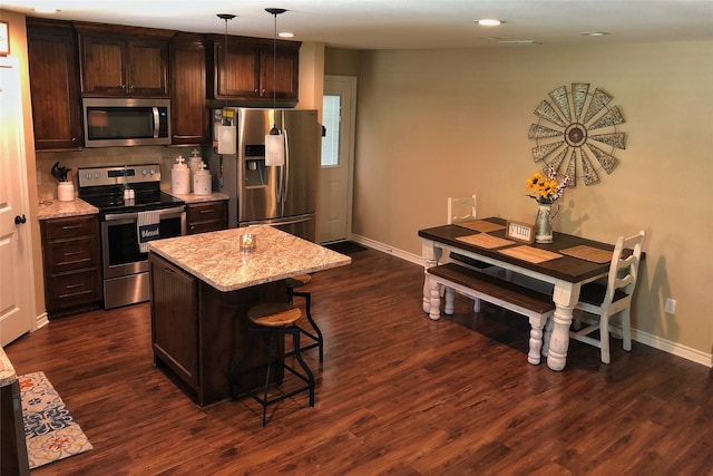 kitchen with dark hardwood / wood-style floors, pendant lighting, a kitchen breakfast bar, stainless steel appliances, and light stone countertops