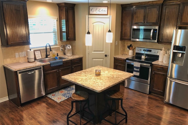 kitchen featuring a kitchen bar, sink, hanging light fixtures, appliances with stainless steel finishes, and a kitchen island