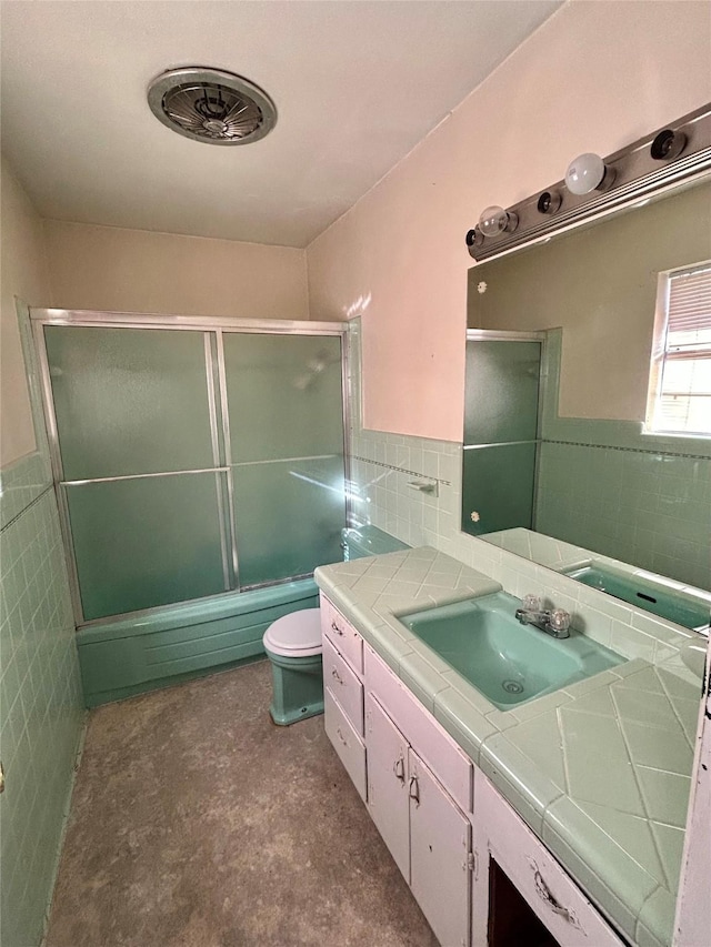 full bathroom featuring enclosed tub / shower combo, vanity, toilet, and tile walls